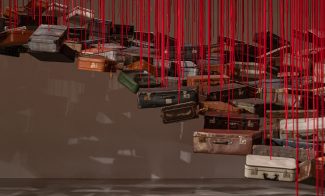 Dozens of suitcases are suspended from the ceiling on red ropes.