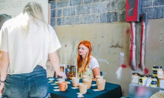 A visitor looks at a table of paintings and pottery in an industrial space