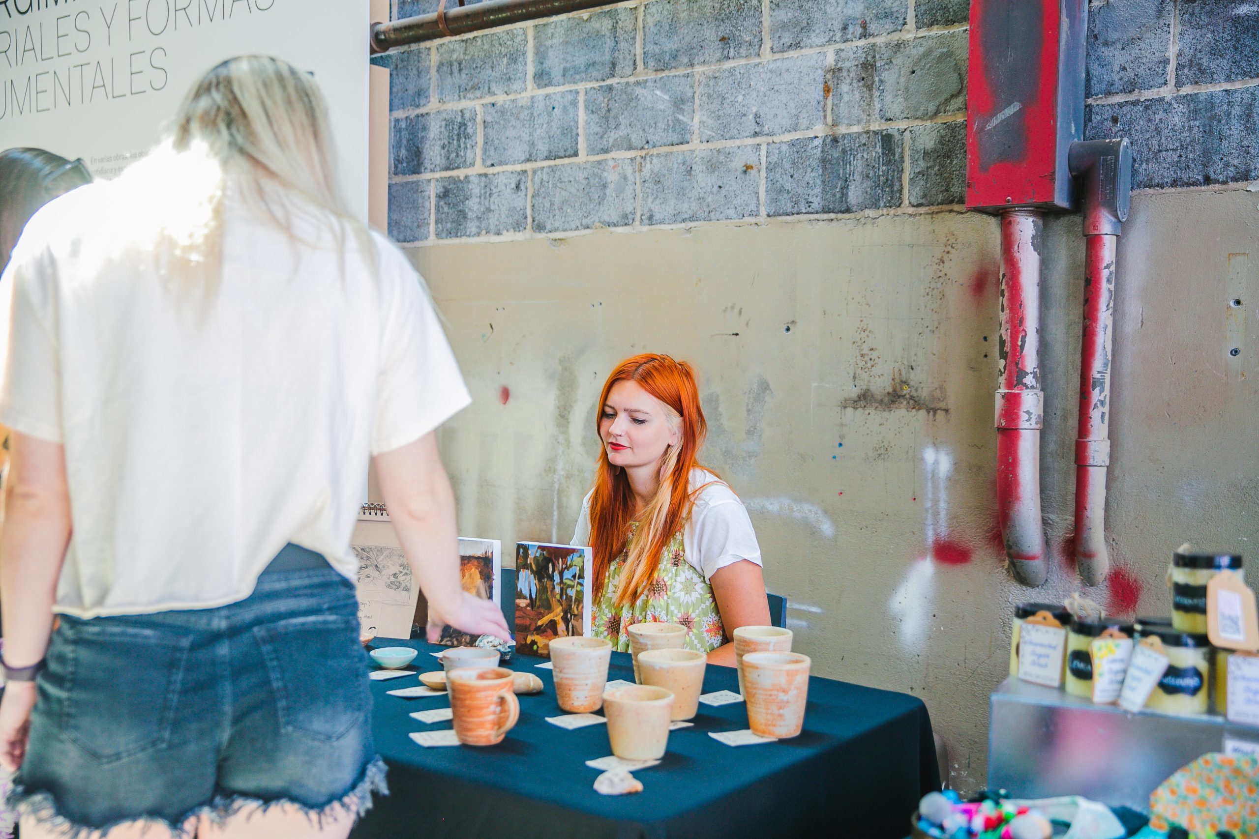 A visitor looks at a table of paintings and pottery in an industrial space