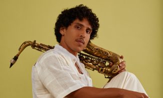 Person in white clothes seated and holding saxophone against yellow background