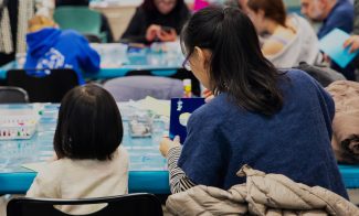 Adults and children gather around tables, deeply engaged in arts and crafts. A logo in corner for Boston Family Days, City of Boston