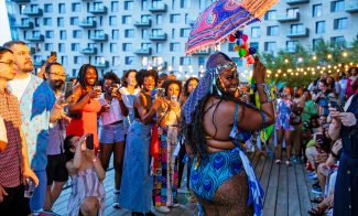 A lively outdoor party with a performer in a colorful outfit holding a decorated umbrella