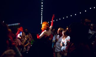 A performer in a red and black outfit entertains an outdoor crowd at night