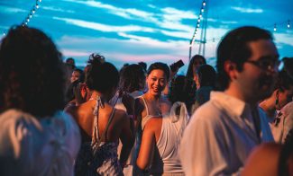 People in all white outfits dance and talk at an outdoor evening party