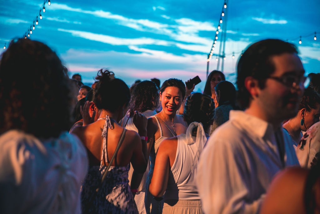 People in all white outfits dance and talk at an outdoor evening party