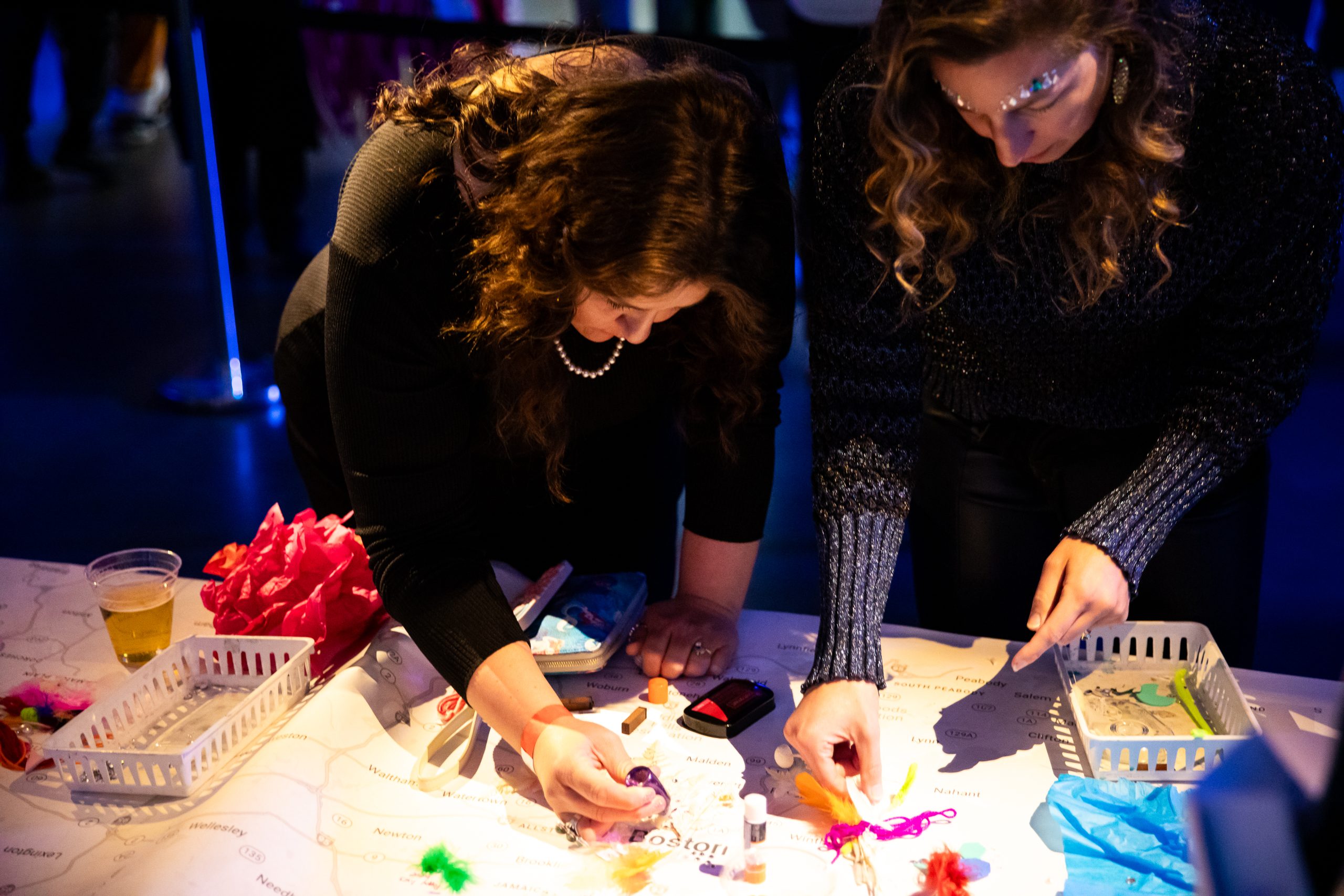 Two people are leaning over a table engaged in an artmaking activity.