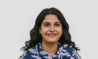 A person with long, dark hair smiles at the camera. They are wearing a blue and white floral patterned shawl.